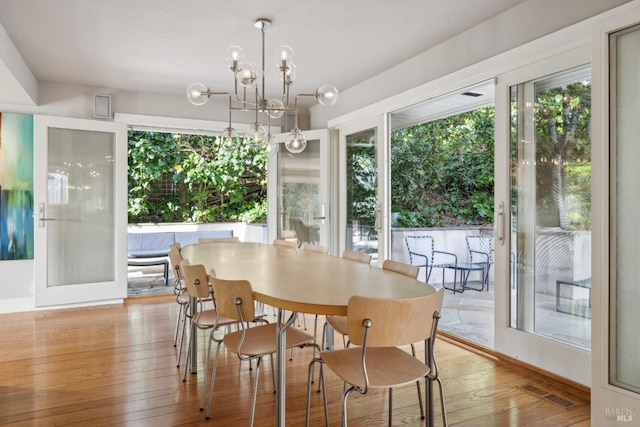 dining area with light wood-type flooring, a notable chandelier, visible vents, and a wealth of natural light