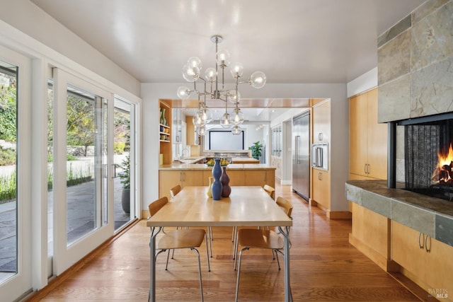 dining area with light wood-style flooring, a fireplace, baseboards, and a notable chandelier