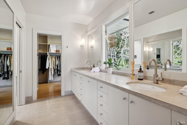 full bath with visible vents, double vanity, a sink, and a walk in closet