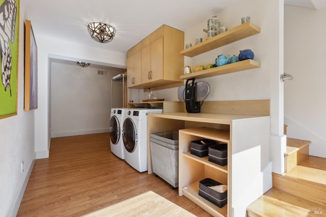 clothes washing area featuring visible vents, baseboards, washer and dryer, light wood-type flooring, and cabinet space