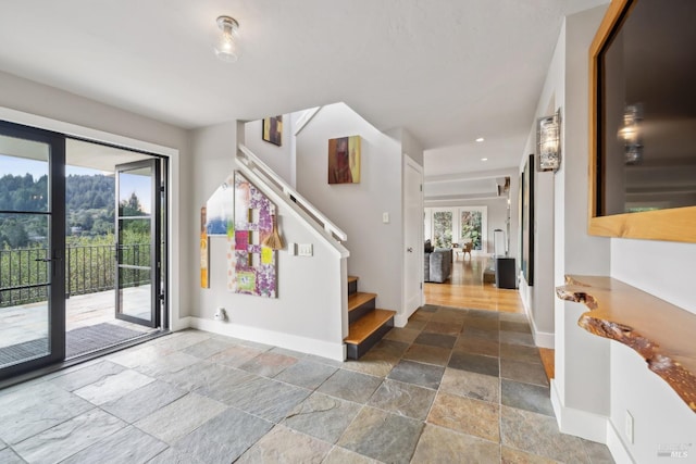 foyer entrance with stairs, a wealth of natural light, stone tile flooring, and baseboards