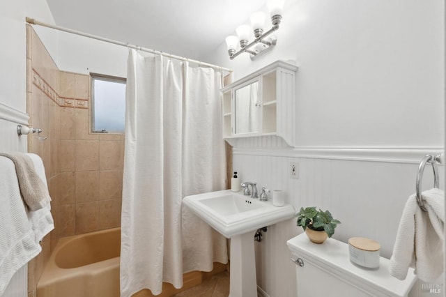 bathroom with a wainscoted wall, shower / bathtub combination with curtain, and toilet