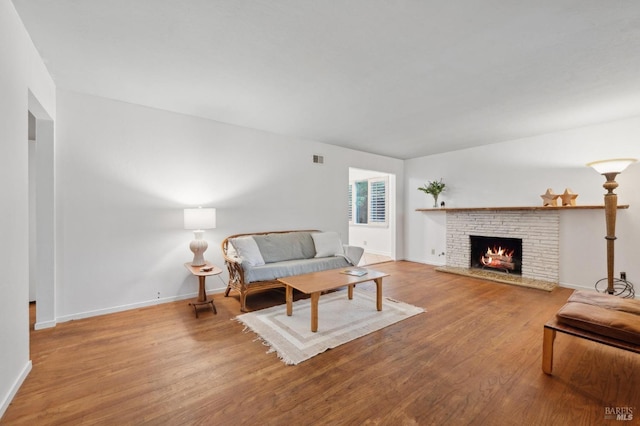 living room featuring a brick fireplace, visible vents, light wood-style flooring, and baseboards