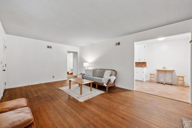 living room with light wood finished floors, visible vents, and baseboards