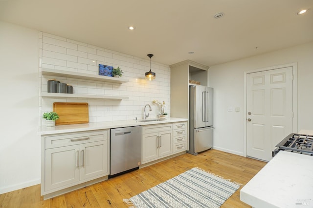 kitchen with light wood-type flooring, stainless steel appliances, pendant lighting, backsplash, and sink