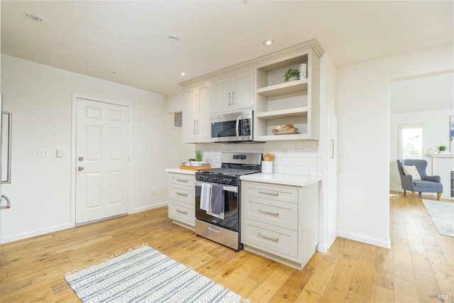 kitchen with light hardwood / wood-style floors, appliances with stainless steel finishes, white cabinetry, and tasteful backsplash