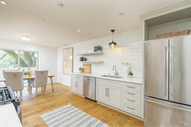 kitchen featuring hanging light fixtures, stainless steel appliances, white cabinets, decorative backsplash, and sink