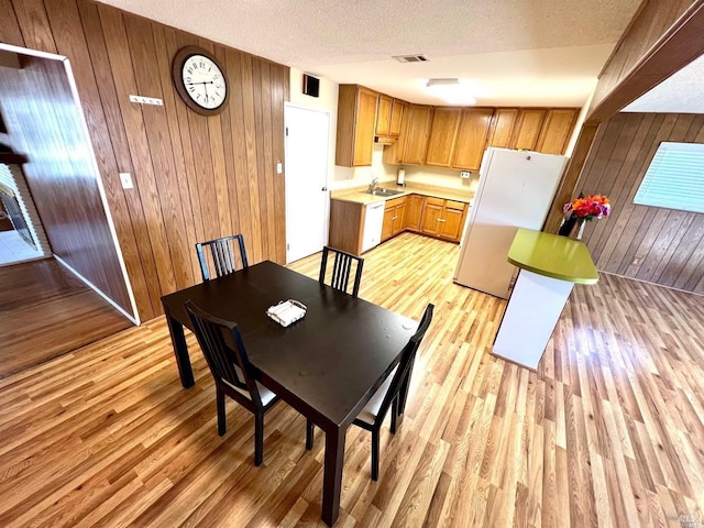 dining space featuring light hardwood / wood-style flooring, sink, a textured ceiling, and wooden walls