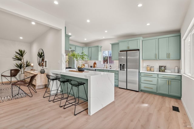 kitchen with light stone counters, a breakfast bar, stainless steel refrigerator with ice dispenser, and light wood finished floors