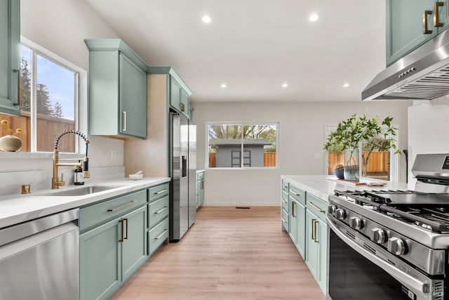 kitchen featuring extractor fan, stainless steel appliances, a sink, light countertops, and light wood finished floors