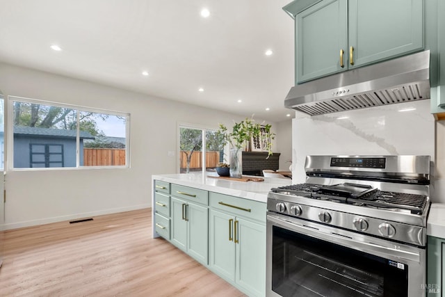 kitchen with stainless steel range with gas stovetop, ventilation hood, light wood-style floors, green cabinetry, and recessed lighting