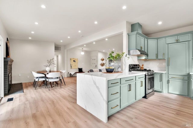 kitchen with green cabinetry, under cabinet range hood, a peninsula, and gas range