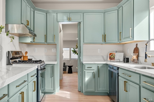 kitchen featuring light stone counters, under cabinet range hood, stainless steel appliances, green cabinets, and light wood finished floors