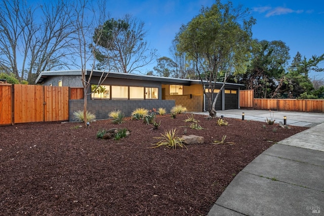 mid-century inspired home with an attached garage, fence, concrete block siding, and concrete driveway