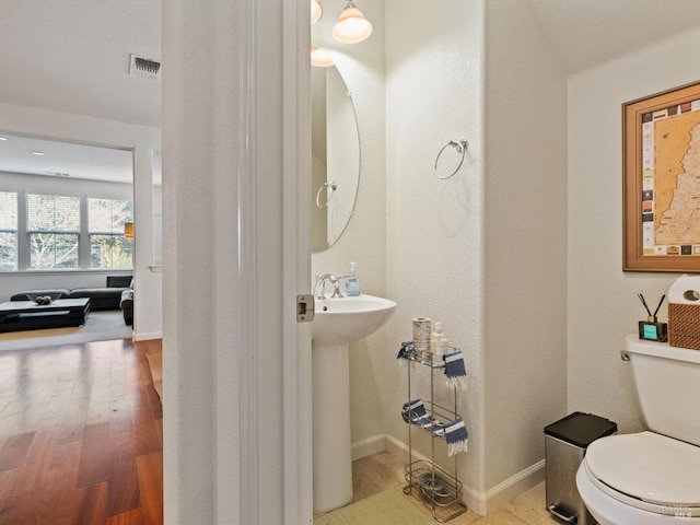 half bathroom with toilet, a sink, wood finished floors, visible vents, and baseboards