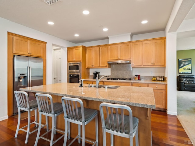 kitchen with a sink, light stone countertops, appliances with stainless steel finishes, and dark wood-type flooring