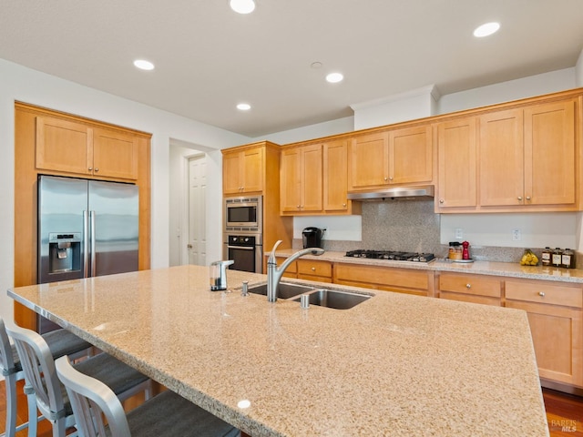 kitchen with recessed lighting, appliances with stainless steel finishes, under cabinet range hood, a sink, and light stone counters