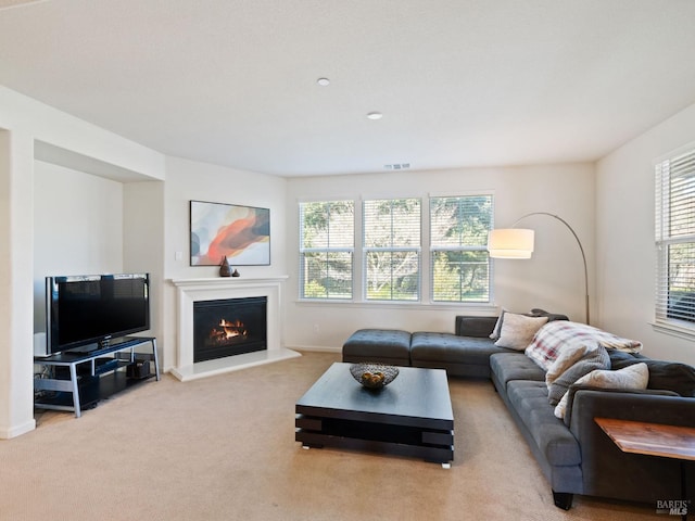carpeted living room featuring baseboards, a lit fireplace, and visible vents