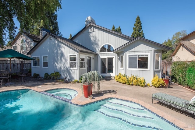 back of house with a chimney, a patio, fence, and an in ground hot tub