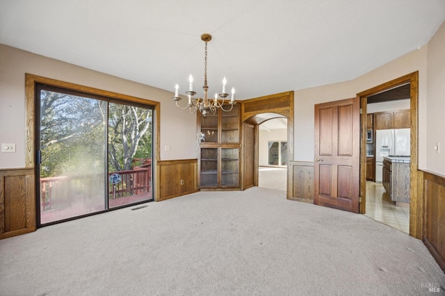 spare room with visible vents, arched walkways, light colored carpet, wainscoting, and a notable chandelier