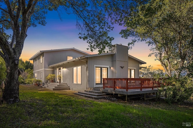 back of house at dusk featuring a deck and a lawn