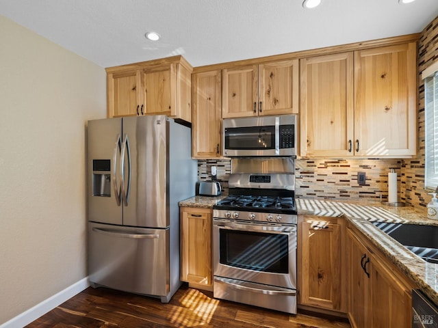 kitchen featuring light stone counters, dark wood-style flooring, tasteful backsplash, appliances with stainless steel finishes, and baseboards