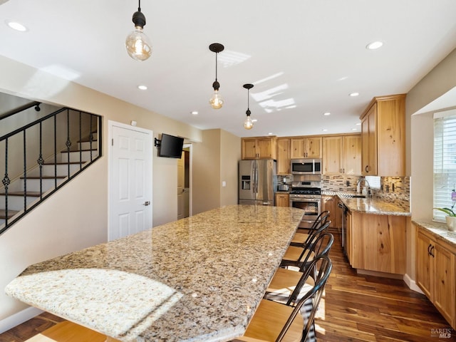 kitchen with stainless steel appliances, a kitchen island, light stone countertops, and pendant lighting