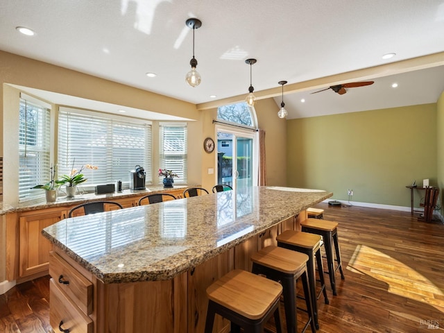 kitchen with baseboards, brown cabinets, dark wood-type flooring, a center island, and hanging light fixtures