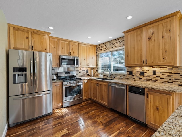 kitchen with decorative backsplash, dark wood finished floors, appliances with stainless steel finishes, light stone counters, and a sink