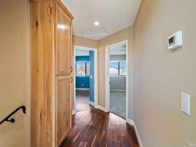 corridor with dark wood-style flooring, attic access, and baseboards