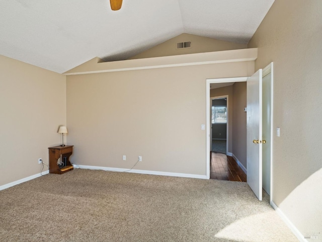 spare room with vaulted ceiling, dark carpet, visible vents, and baseboards