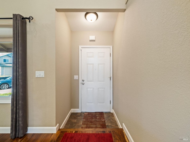 doorway with dark wood-style floors, a textured wall, and baseboards