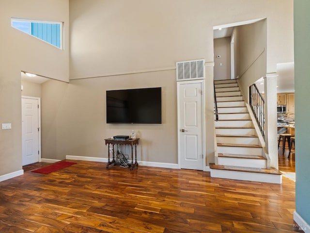 unfurnished living room featuring a high ceiling, dark wood-style floors, stairs, and visible vents