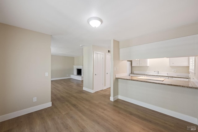 kitchen featuring white cabinetry, a brick fireplace, sink, light stone counters, and wood-type flooring