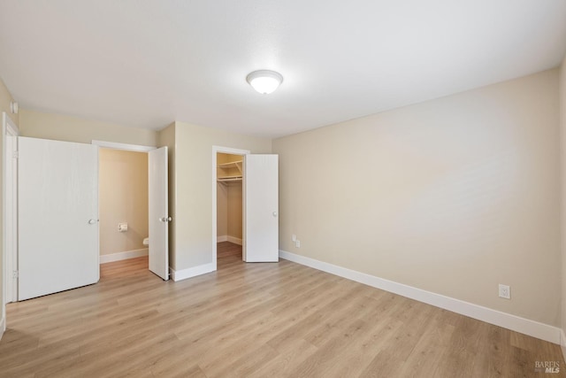 unfurnished bedroom with light hardwood / wood-style floors, a closet, and a walk in closet