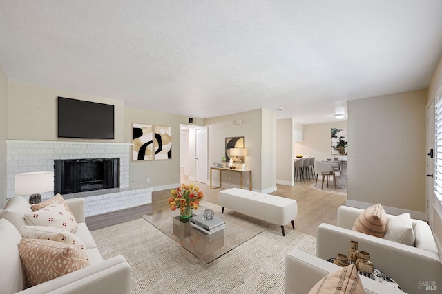 living room with light hardwood / wood-style floors, a brick fireplace, and a textured ceiling