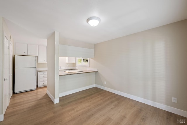 kitchen with kitchen peninsula, white cabinets, white fridge, and light hardwood / wood-style flooring