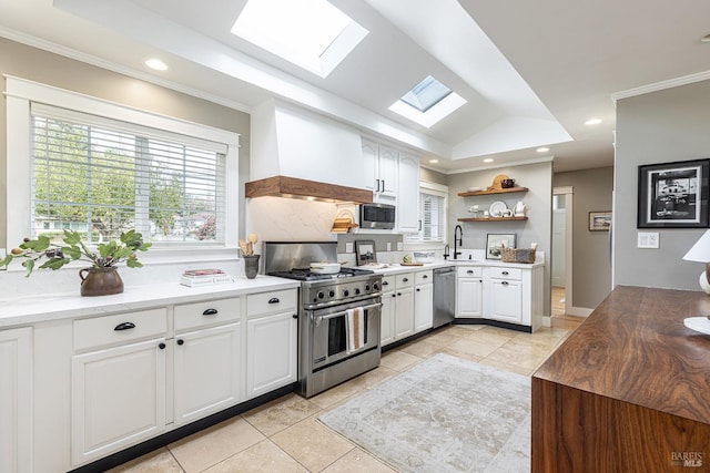 kitchen featuring stainless steel appliances, premium range hood, sink, white cabinets, and vaulted ceiling with skylight