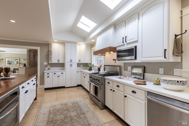 kitchen with vaulted ceiling with skylight, white cabinetry, stainless steel appliances, and custom range hood