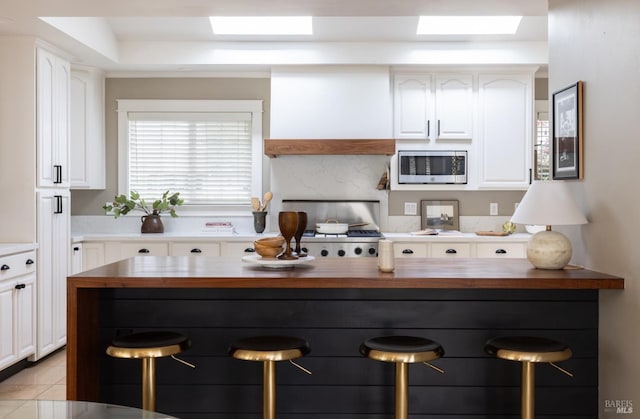 kitchen with white cabinets, stainless steel microwave, a breakfast bar, and butcher block countertops