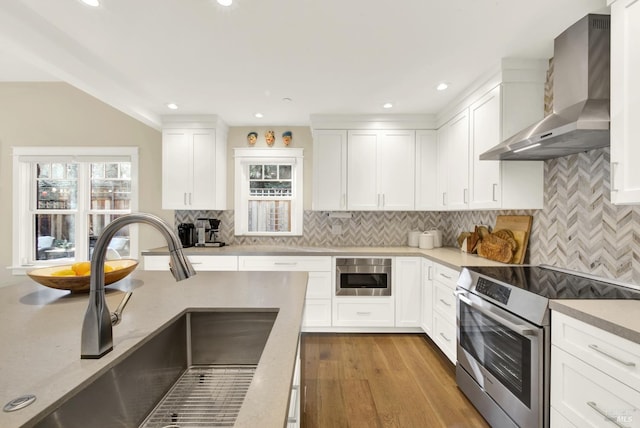 kitchen featuring light wood finished floors, stainless steel appliances, white cabinets, a sink, and wall chimney range hood