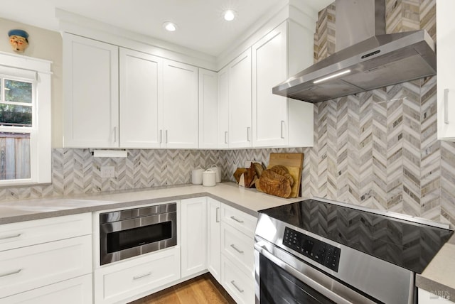 kitchen featuring stainless steel appliances, light countertops, wall chimney exhaust hood, and white cabinetry