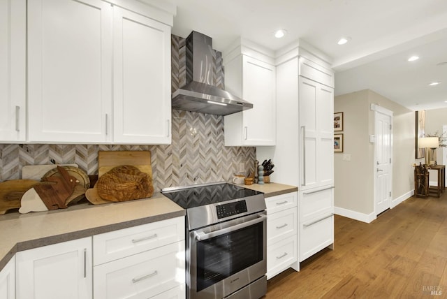 kitchen with wall chimney range hood, white cabinetry, stainless steel electric stove, and backsplash