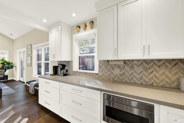 kitchen featuring decorative backsplash, white cabinets, stainless steel microwave, vaulted ceiling, and light countertops