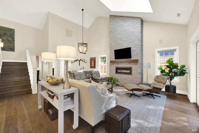 living area featuring high vaulted ceiling, a stone fireplace, wood finished floors, visible vents, and stairway