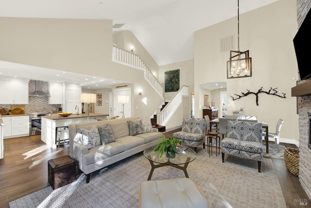 living room featuring high vaulted ceiling, a stone fireplace, wood finished floors, visible vents, and stairway