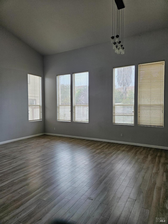 unfurnished room featuring a chandelier, dark wood finished floors, and baseboards