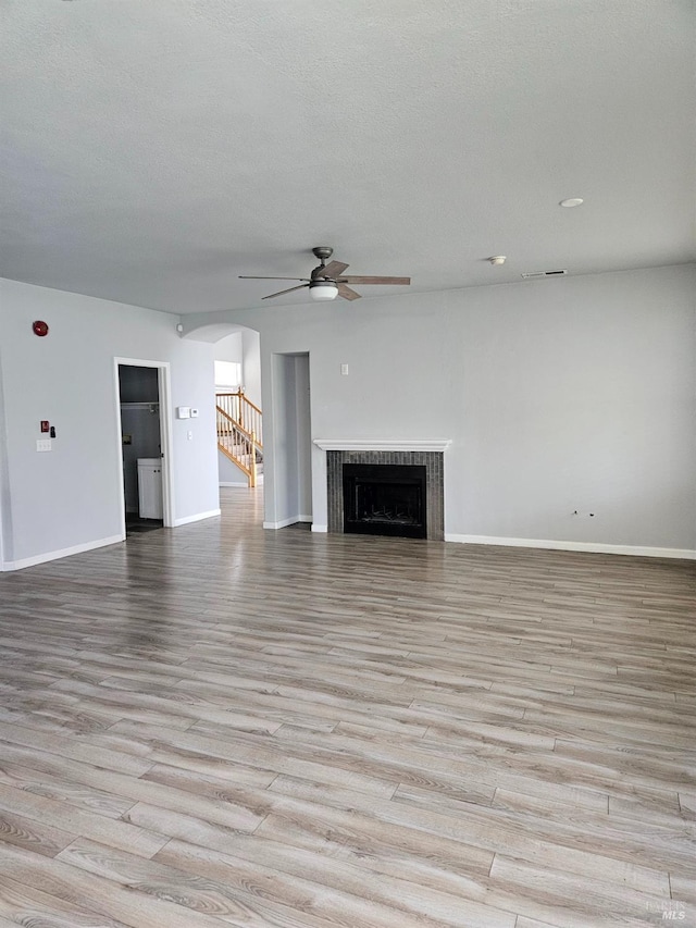 unfurnished living room with arched walkways, a fireplace, a textured ceiling, and light wood finished floors