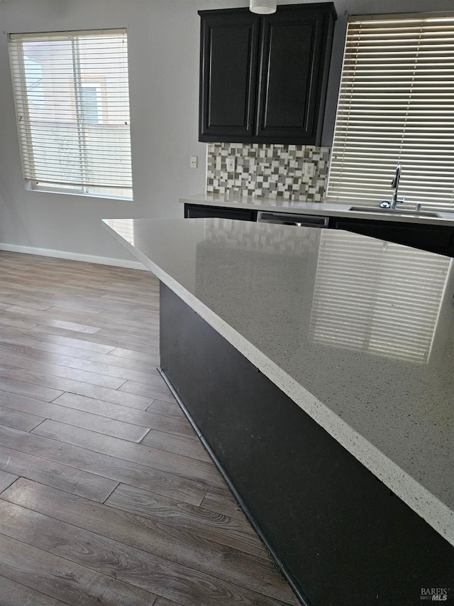 kitchen featuring light wood-style flooring, a sink, baseboards, dark cabinetry, and backsplash