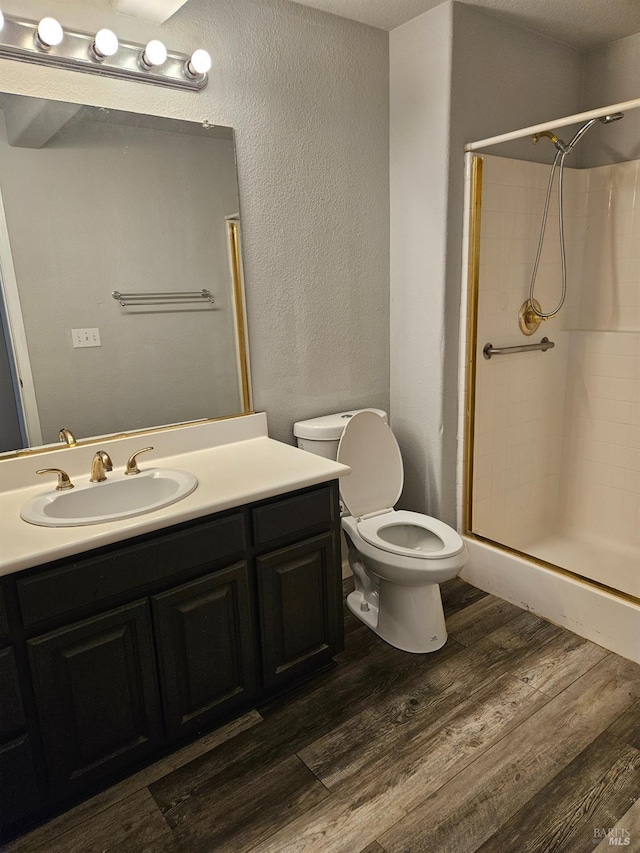 bathroom with a textured wall, toilet, wood finished floors, vanity, and a shower stall